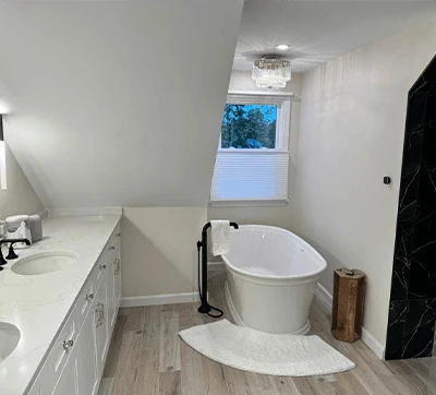 Modern bathroom with a freestanding white bathtub, marble counters, a window, and sleek black fixtures.