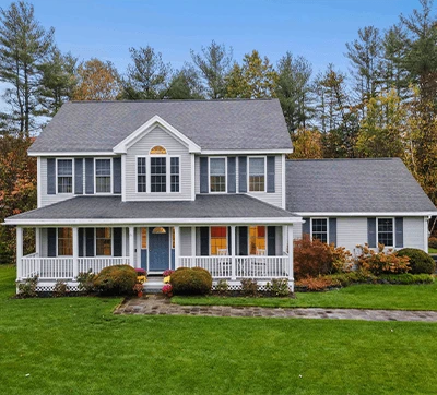 Large two-story white house with blue shutters and a connected garage, surrounded by autumn trees and a well-manicured lawn.